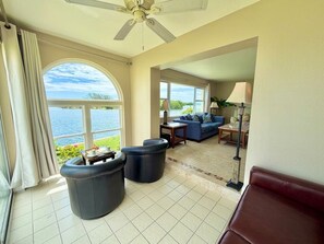 A spacious room with a large window, a ceiling fan, a sofa, a coffee table, and a lamp. - Spanish Trace Escape | Pool + Minutes to the Beach (Cocoa Beach)