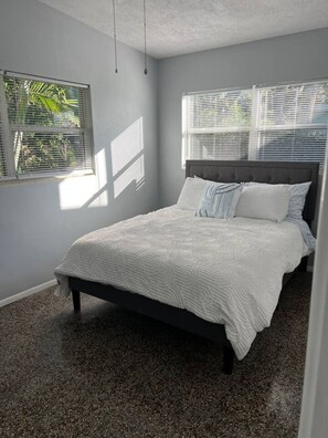 Ein Schlafzimmer mit einem Bett, zwei Fenstern mit Jalousien, einer Deckenleuchte und einem Teppichboden.