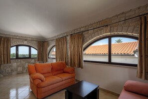 Ein Zimmer mit Steinwand, einer Couch, einem Tisch und großen Fenstern mit Vorhängen.