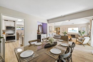 A modern kitchen with built-in appliances, a dining area with a wooden table set for four, and a living room with a sofa and TV. - Sea Pines 3BR, Pet-Friendly, South Beach Pool Access, Bike to Beach & Golf! (Hilton Head Island)