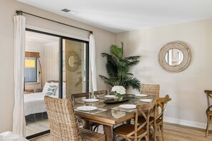 A dining area with a glass table, wicker chairs, and a potted plant. - Sea Pines 3BR, Pet-Friendly, South Beach Pool Access, Bike to Beach & Golf! (Hilton Head Island)