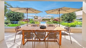 Een zonnig buitendinergedeelte met uitzicht op het zwembad, met een houten tafel, rieten stoelen en grote parasols.