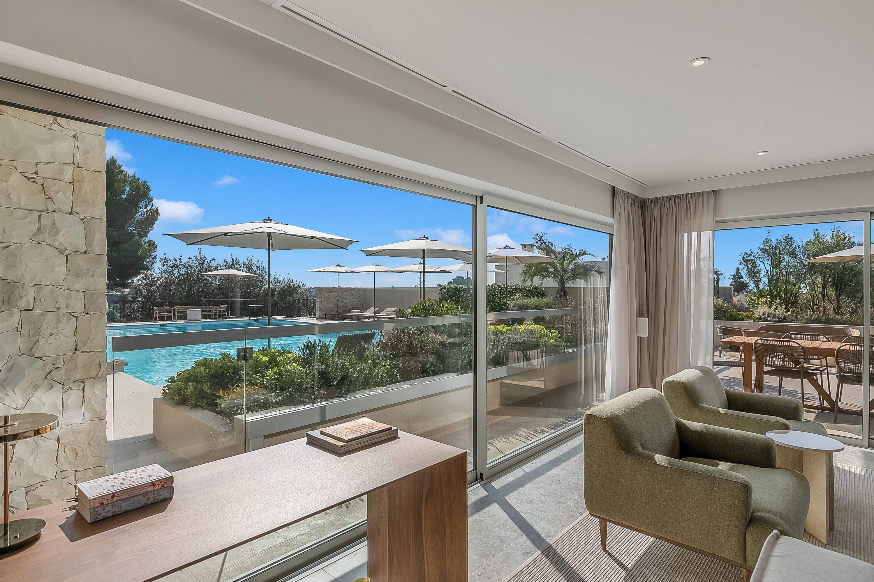 Ein modernes Hotelzimmer mit großem Fenster, Blick auf den Pool und einer Sitzecke mit Tisch und Stühlen.