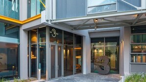 Un bâtiment moderne doté d’une façade en verre, d’une grande sculpture représentant le chiffre « 3 » et d’un espace d’entrée pavé.