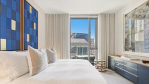 Une chambre d’hôtel avec un grand lit, une vue sur la ville, un coin repas et une grande fenêtre avec des rideaux.