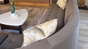 Un soggiorno moderno con un'ampia televisione a schermo piatto, un divano grigio con cuscini decorati, un piccolo tavolino con un cactus e un grande quadro astratto appeso alla parete.