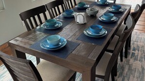 Une table à manger dressée avec de l’assiette et des bols bleus, des chaises en bois et des lampes suspendues.
