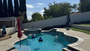 Une piscine avec un jacuzzi, entourée d’une terrasse en pierre et d’un mur blanc.