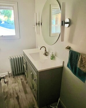 Ein Badezimmer mit einem weißen Waschbecken, einem Spiegel, einem Handtuchhalter und einer Heizung.