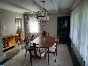 Ein Esszimmer mit Holztisch, sechs Stühlen, einer Kandelaber, einem Schrank und einem Fenster mit Vorhängen.