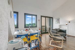 A dining area with a table set for four, a blue and yellow chair, a grey sofa, and a floor lamp. - Oasi nel Parco - Hillside Home with Shared Pool, Gignese, Italy (Gignese)