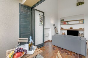 Ein Wohnbereich mit grauem Sofa, einem Tisch mit Früchten und einer Flasche, einer Schiebetür und einem Bücherregal mit Büchern und Dekoration.