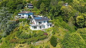 Une propriété située sur une colline, comprenant plusieurs maisons, une végétation luxuriante et une maison imposante dotée d’un toit équipé de panneaux solaires.