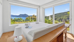 Une chambre moderne avec un grand lit, une table de chevet avec une lampe, et une vue sur un paysage montagneux grâce à de grandes fenêtres.