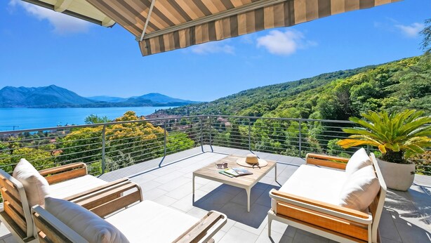 Une terrasse offrant une vue sur un lac et des montagnes, aménagée avec une table, des chaises et un pot de fleurs.