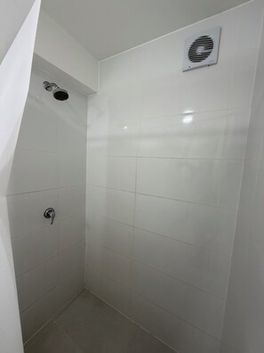 A small, enclosed shower area with white tiles, a showerhead, and a ventilation fan.
