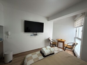 A hotel room with a bed, a television mounted on the wall, a small table with chairs, and a window with blinds. - Studio apartment (San Miguel)