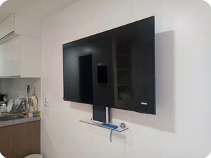 A modern kitchen with a flat-screen TV mounted on the wall, a glass shelf below, and a sink with dishes.