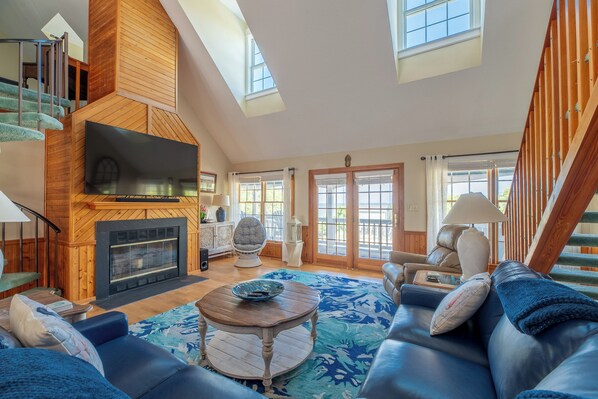 A spacious living area with a fireplace, a large TV, and a staircase leading to an upper level. - The Virginian at Duck - Sound Sea Village, Sound Views, Private Dock, Pets OK, Flex Stays (Duck)