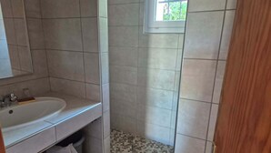 A bathroom with a sink, mirror, shower, and a window.