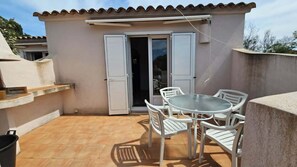 A small patio with a round table and white chairs, a sliding glass door, and a tiled floor. - MINI Villa in Santa Giulia 4 (Porto-Vecchio)