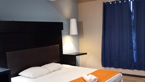 Een hotelkamer met een bed, nachtkastje, lamp en raam met gordijnen.