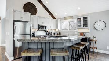 Una cocina con una isla central, taburetes de bar, refrigerador, microondas y un reloj en la pared.