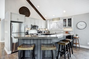 A kitchen with a central island, bar stools, a refrigerator, microwave, and a clock on the wall. - Downtown Breckenridge retreat with mountain views, fireplace, hot tub. (Breckenridge)