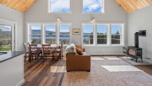 Amplia sala de estar con techo alto, ventanas grandes, chimenea y comedor con sillas y mesa.