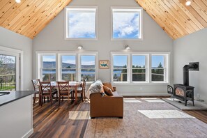 Ein geräumiges Wohnzimmer mit hohen Decken, großen Fenstern, einem Kamin und einem Essbereich mit Stühlen und Tisch.