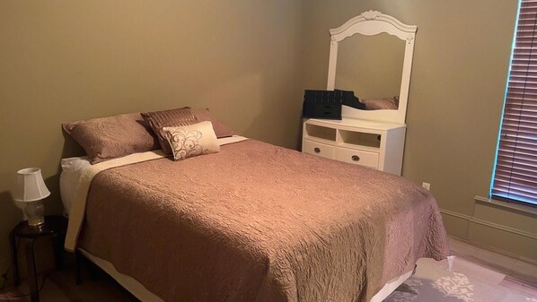 Un dormitorio con cama, mesita de noche, cómoda, espejo y ventana con persianas.