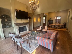 Una sala de estar con chimenea, sofá, sillones, una mesa de centro y un televisor sobre la chimenea.