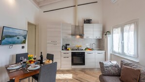 Une cuisine moderne avec des meubles blancs, un coin repas avec une table dressée pour deux personnes, et un canapé agrémenté de coussins à motifs.