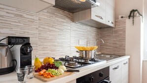 Une cuisine moderne équipée d’une cuisinière à gaz, d’une bouilloire, d’une planche à découper avec des légumes et d’un panier de fruits.