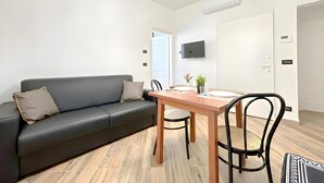Ein modernes Wohnzimmer mit einer schwarzen Couch, einem Holzesstisch und einem an der Wand befestigten Fernseher.