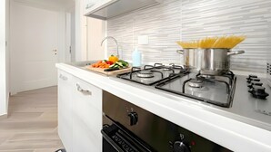 Eine moderne Küche mit weißer Arbeitsplatte, zwei Gasherden, einem Topf Spaghetti und einem Schneidebrett mit Gemüse.