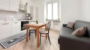 Eine moderne Küche mit weißen Schränken, einem Esstisch mit Stühlen, einer schwarzen Couch und einem Fenster mit Vorhängen.