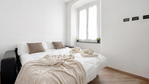 Ein Schlafzimmer mit einem Bett, einem Fenster, einem Nachttisch und einem Wandregal mit Pflanzen.