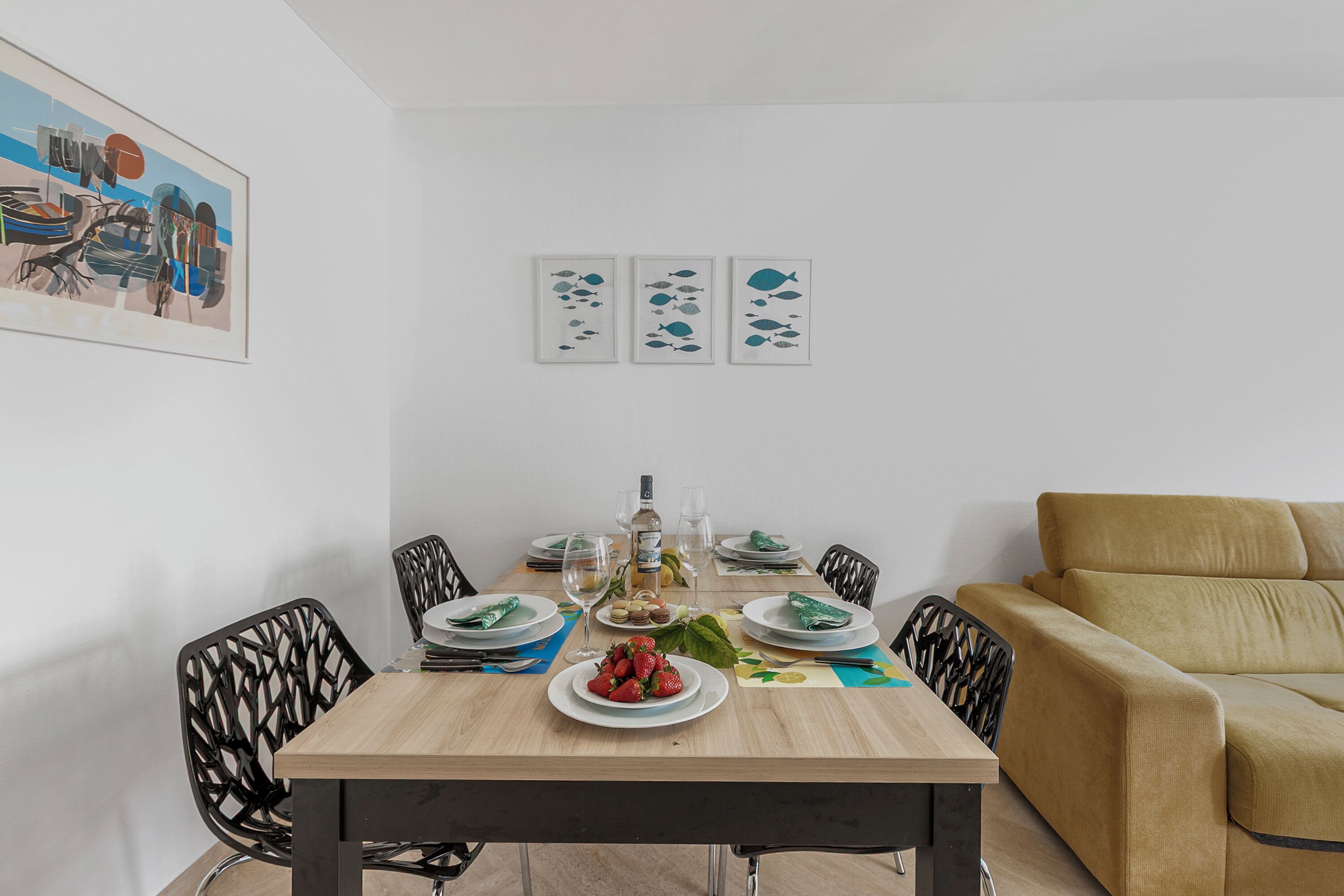 A dining area with a wooden table, black chairs, a sofa, and wall art.