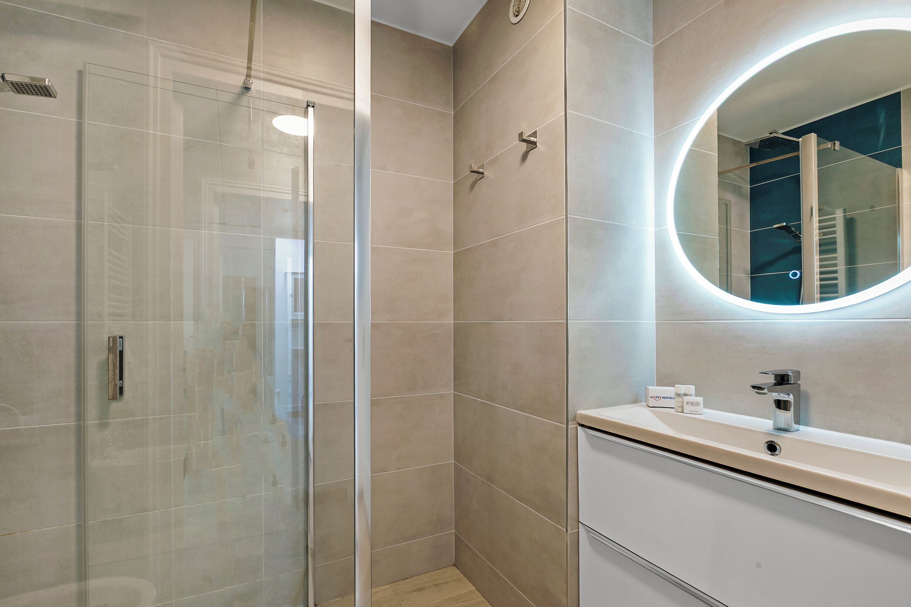 A modern bathroom with a glass shower enclosure, a round mirror, and a vanity with a sink.