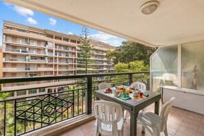 Ein Balkon mit Tisch und Stühlen, mit Blick auf ein Wohnhaus mit mehreren Balkonen.