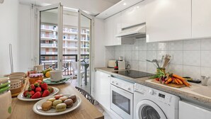 Eine moderne Küche mit Waschmaschine, einem Essbereich mit gedecktem Tisch und Blick auf ein Wohnhaus durch eine offene Tür.