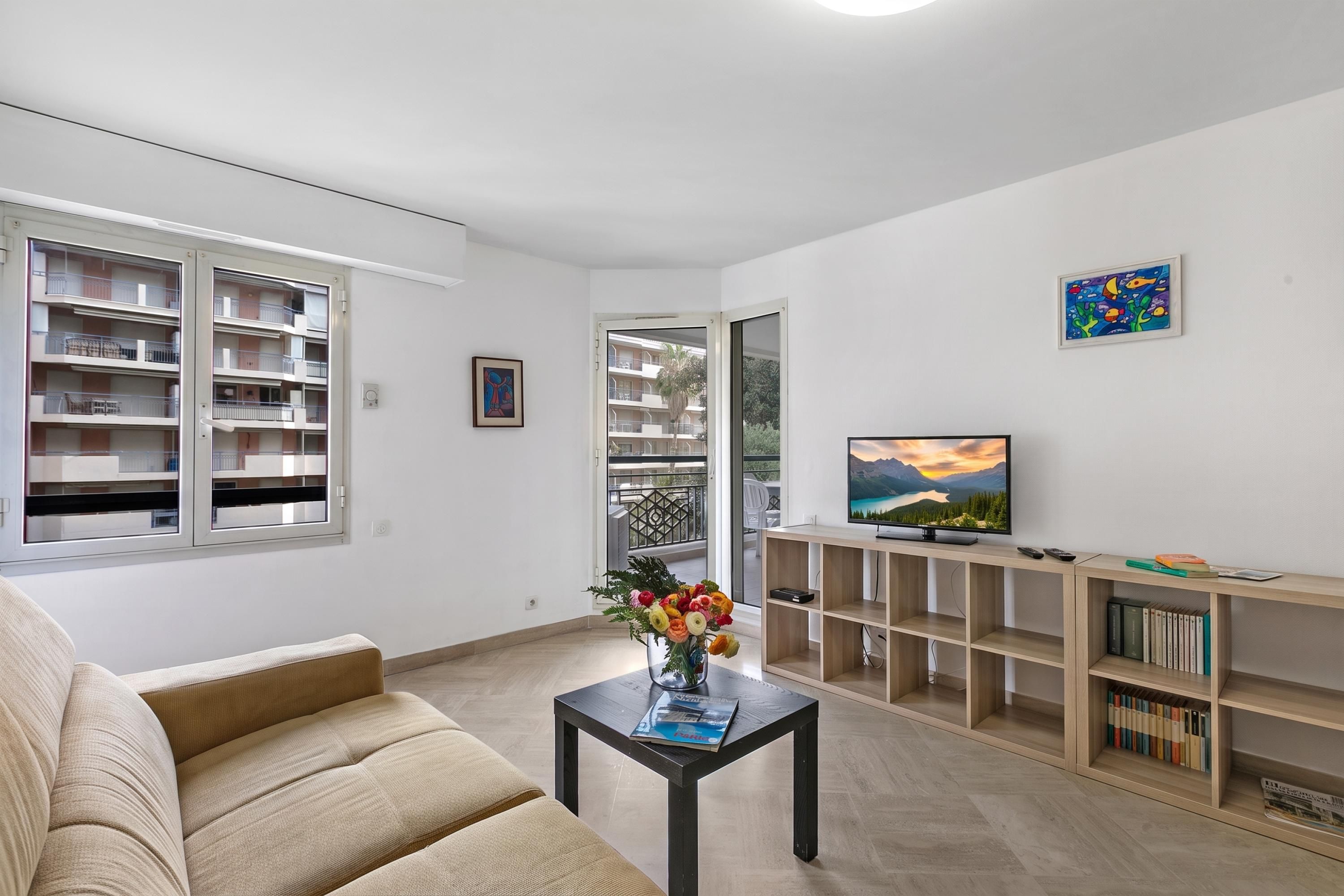 Una sala de estar con un sofá, una mesa de centro con una revista, un televisor sobre un mueble de madera y una estantería.