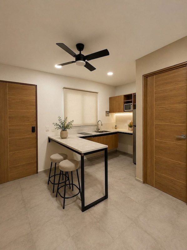 Une cuisine moderne dotée d’un îlot central, de tabourets de bar, d’un ventilateur de plafond et de meubles de rangement en bois.