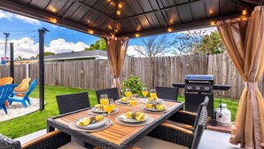Een terras buiten met een overdekte eethoek, een barbecue en zitplaatsen.