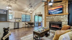 Una cocina moderna con armarios blancos, un comedor con mesa y sillas, una chimenea y una sala de estar con sofá y una decoración de oso.