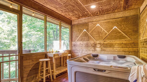 Una cabaña de madera con jacuzzi, taburetes de madera y una ventana con vistas a follaje.