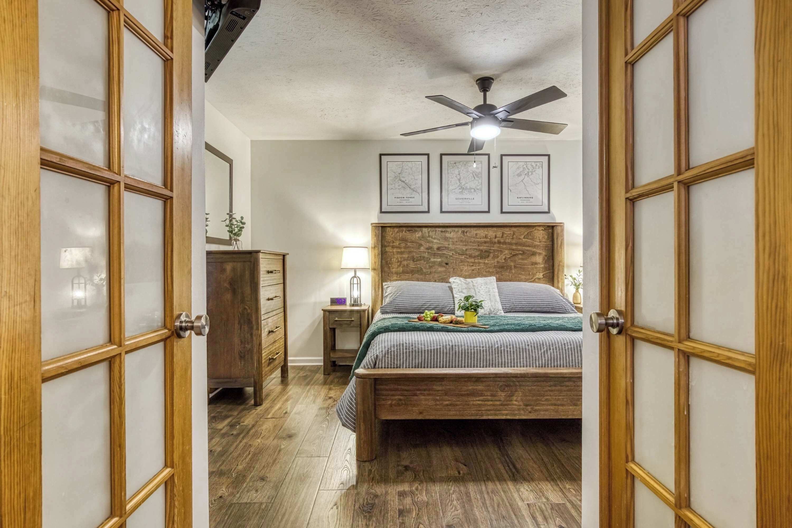 A bedroom with a wooden bed, a ceiling fan, and framed maps on the wall.