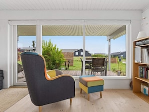 A room with a large sliding glass door leading to a patio, a chair, a small ottoman, and a bookshelf. - 4 Star Holiday Home in Bogense (Bogense)