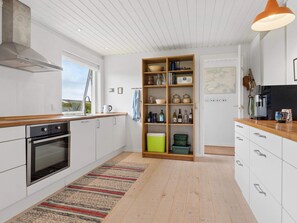 A modern kitchen with white cabinetry, a built-in oven, a coffee machine, and a wooden shelf unit. - 4 Star Holiday Home in Bogense (Bogense)
